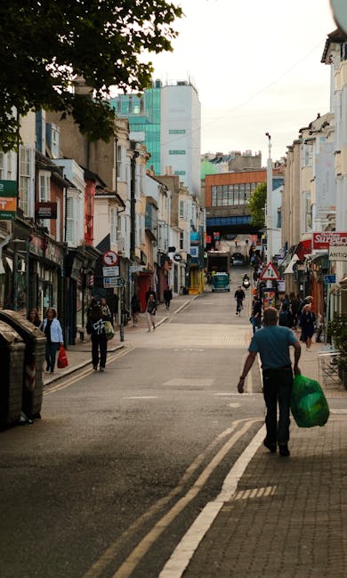 A black wheeled rubbish bin positioned on the pavement beside a road at night, labeled with the name 'St. John's'. The bin is filled with various waste materials, including cardboard boxes, paper, and